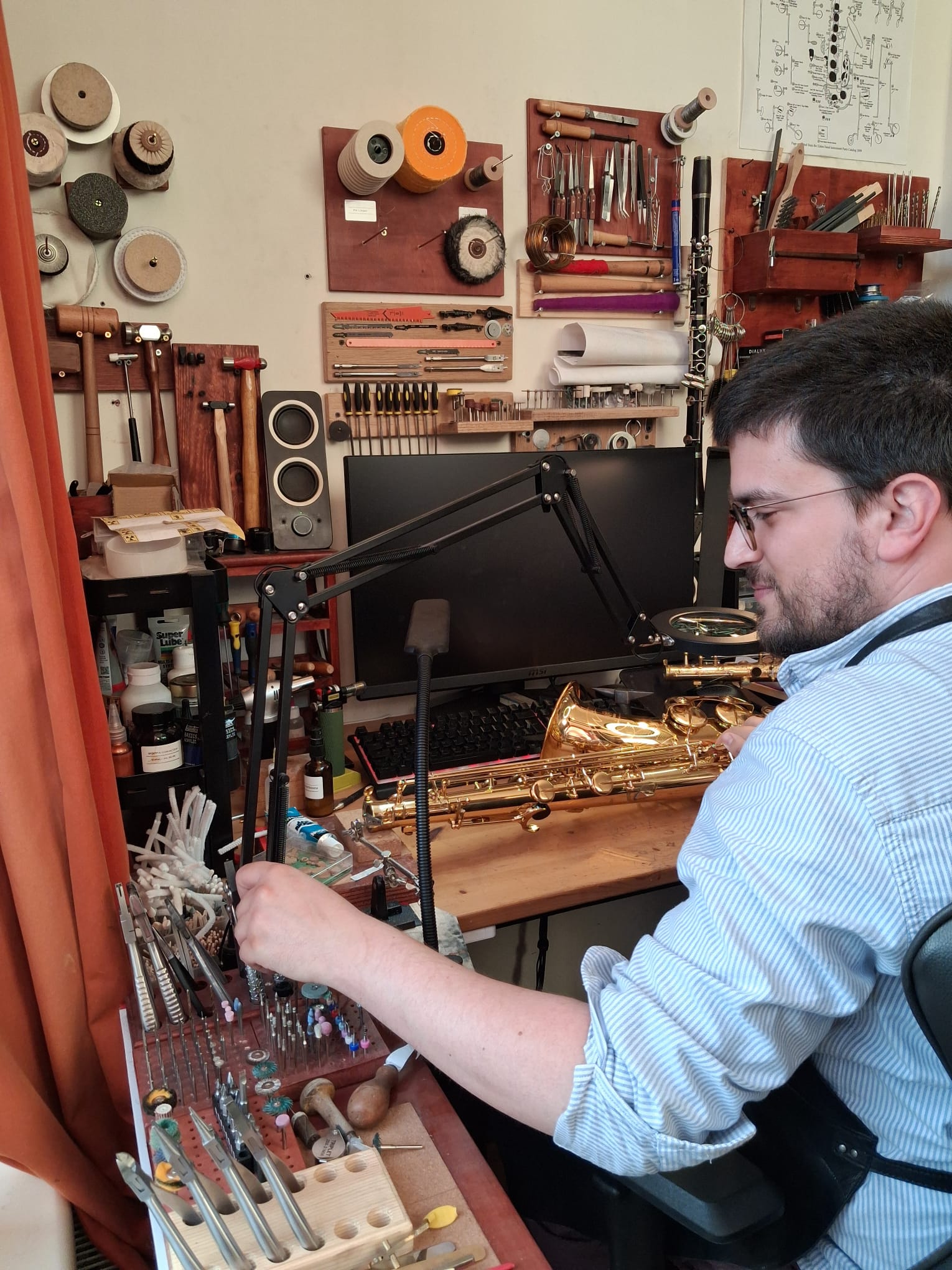 Antonio Jara at his repair bench in the workshop, working on a saxophone surrounded by tools